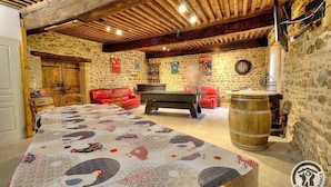 Une pièce au décor rustique, avec un billard, un canapé en cuir rouge, des murs en pierre et des poutres en bois.