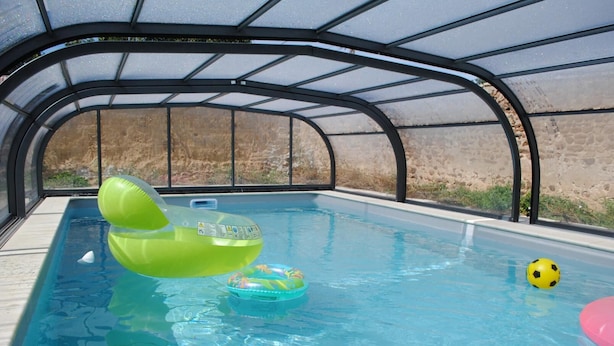Une piscine entourée de parois en verre, des bouées gonflables et un ballon jaune.