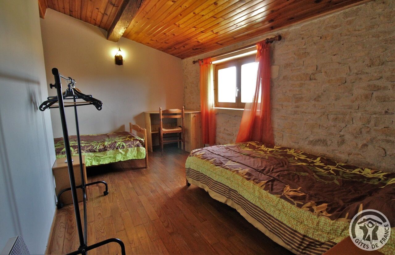 Una habitación rústica con techo de madera, una cama con cubrecama estampado, una silla, un perchero y una ventana con cortinas.