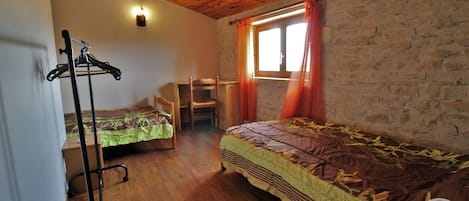 Una habitación rústica con techo de madera, una cama con cubrecama estampado, una silla, un perchero y una ventana con cortinas.