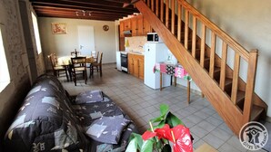 A cozy living room with a sofa, a dining table with chairs, a kitchen area with a microwave and refrigerator, and a wooden staircase. - Gîte Passot - MORANCE - Gîte (MORANCE)
