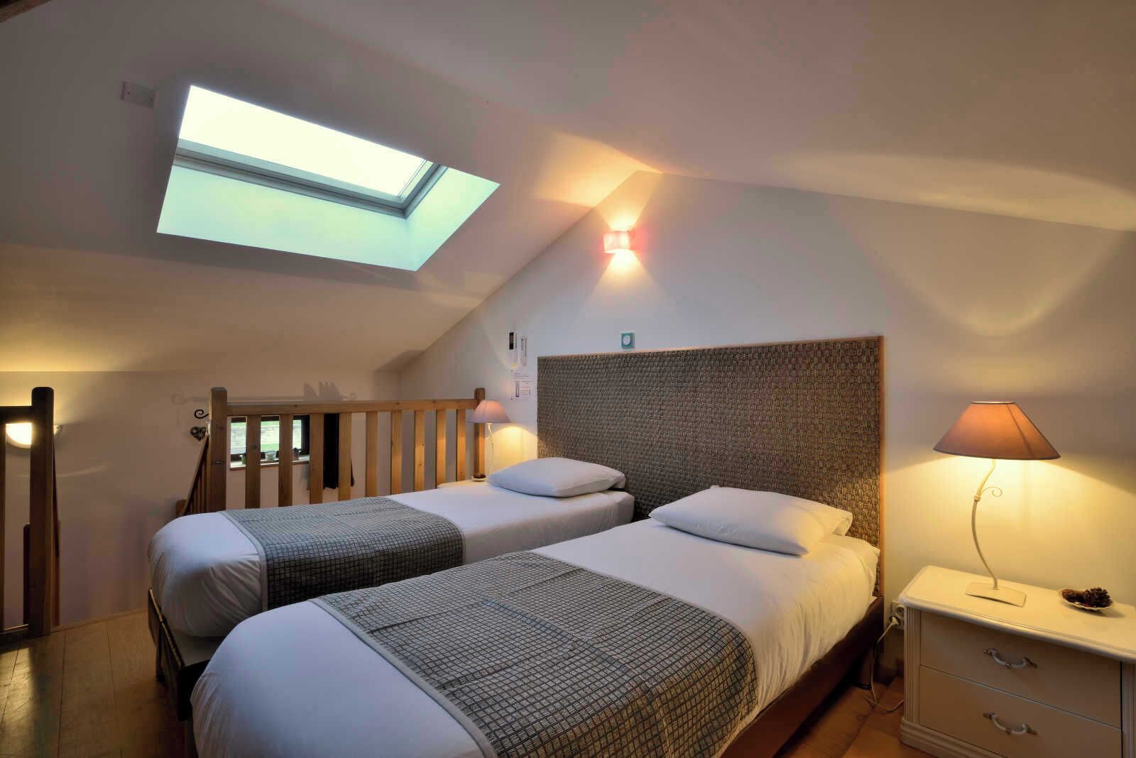 A room with two beds, a skylight, a headboard, a nightstand, and a lamp.