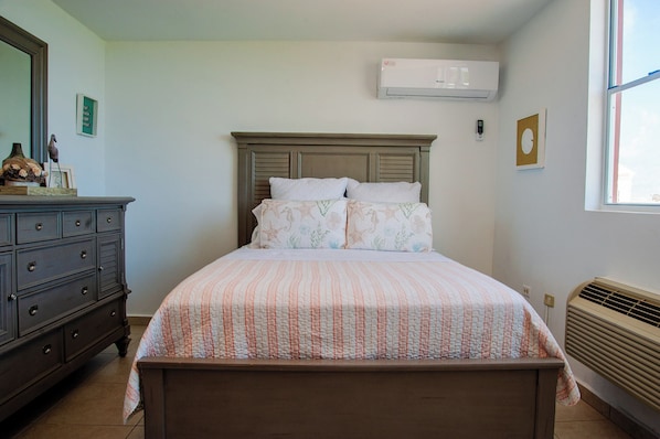 A bedroom with a bed, dresser, and an air conditioning unit. - El Combate Oceanview Condos (Boquerón)