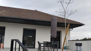 Una casa moderna con techo de tejas, un porche cubierto con mobiliario exterior y un pequeño árbol.
