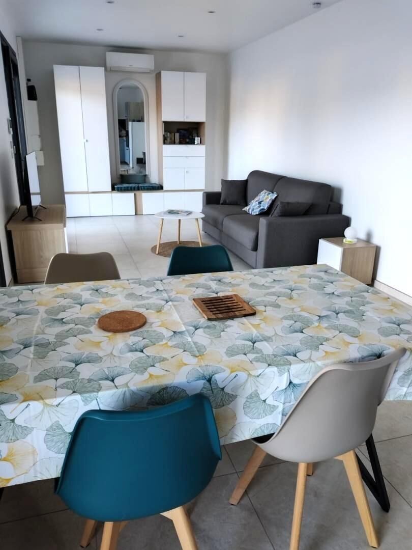 Un coin repas avec une table dressée pour quatre personnes, un canapé et une cuisine en arrière-plan.