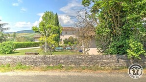 Un mur de pierre, un bâtiment avec un toit en tuiles et un arbre aux feuilles vertes.
