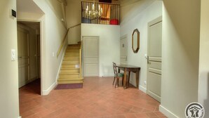 A spacious hallway with a staircase leading to a balcony, a dining area with a table and chairs, and a door on the right.