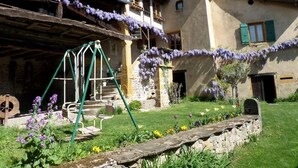 Ein rustikales Gebäude mit einer Steintreppe, einer Schaukel und einem Garten mit verschiedenen Blumen.