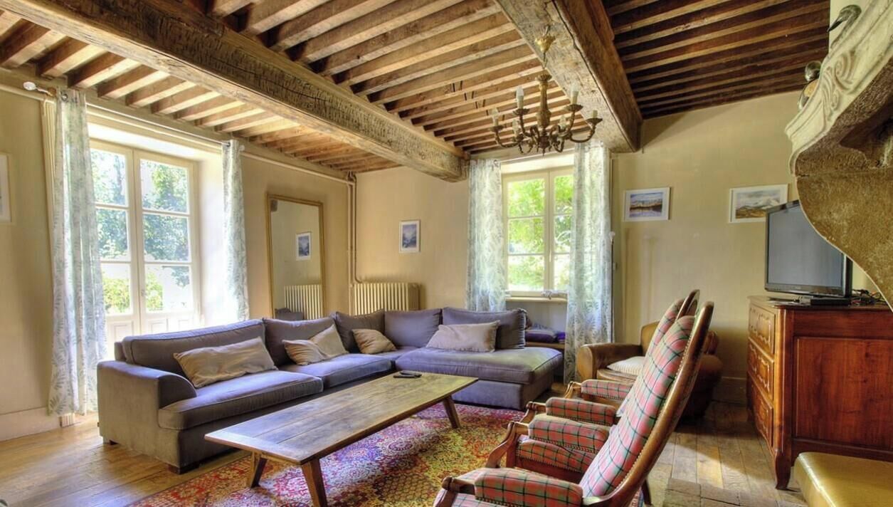 Quarto com um amplo sofá modular, uma mesa de centro e poltronas xadrez. Há uma televisão sobre um móvel de madeira.