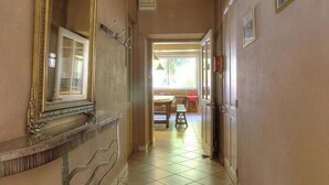 Ein Flur mit einem großen, verzierten Spiegel, einer Leuchte und einer Tür zu einem Zimmer mit einem Fenster.