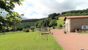 Une propriété rurale comprenant un bâtiment en pierre, une aire de jeux et une pelouse bien entretenue.