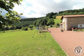 Ein ländliches Anwesen mit einem Steinhaus, einem Spielplatz und einem gepflegten Rasen.