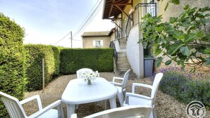 A small outdoor seating area with a table and chairs, a staircase leading to a building, and a hedge in the background.