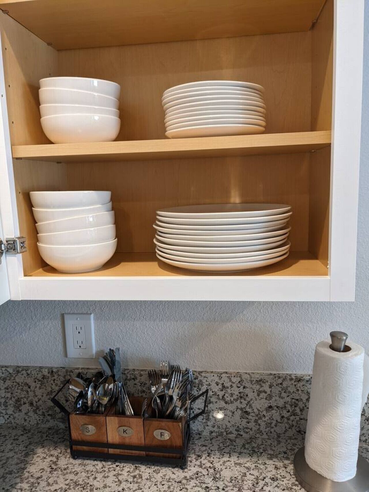 Eine Küche mit Holzausstattung, weißem Geschirr und einer Utensilienablage auf der Arbeitsplatte, sowie einem Papierhandtuchspender.