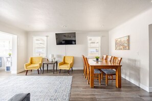 A spacious living room with a large wooden dining table, yellow armchairs, and a grey rug. - #717 Charming 4-Bed Midtown Reno Retreat (Reno)