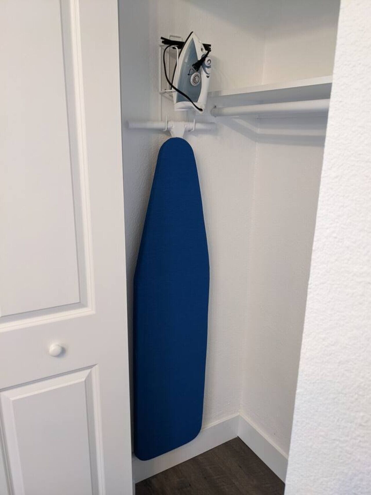 Canto de um quarto com uma porta branca, um ferro de passar azul e um suporte de ferro de passar na parede.