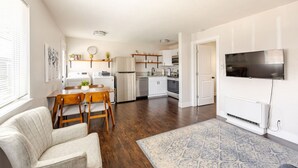 A modern kitchen with white cabinets, a built-in oven, and a refrigerator. There is a dining area with a wooden table and chairs, and a TV mounted on the wall. - #719 Cozy Midtown Reno Retreat (Reno)