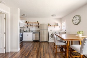 Una cuina moderna amb sòl de fusta, armaris blancs, rentaplats integrat, frigorífic i zona de dinar amb taula i cadires de fusta.