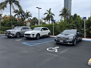 A parking lot with three cars, including a Mercedes-Benz, and a disabled parking sign. - Walk to Beach! Spacious Family Condo w/ Pool, Gym & Parking (Sunny Isles Beach)