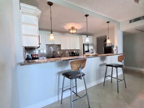 A kitchen with white cabinets, a marble countertop, and two bar stools. - Walk to Beach! Spacious Family Condo w/ Pool, Gym & Parking (Sunny Isles Beach)