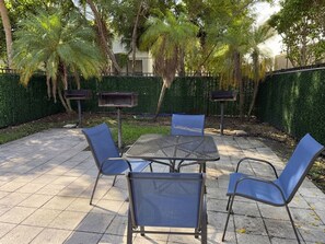 An outdoor patio with a table and chairs, surrounded by a hedge and trees. - Walk to Beach! Spacious Family Condo w/ Pool, Gym & Parking (Sunny Isles Beach)