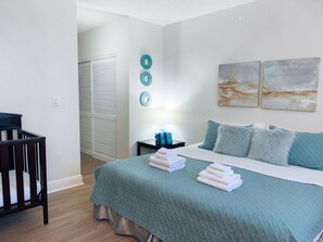 A bedroom with a bed, a crib, a nightstand, and wall art. - Walk to Beach! Spacious Family Condo w/ Pool, Gym & Parking (Sunny Isles Beach)