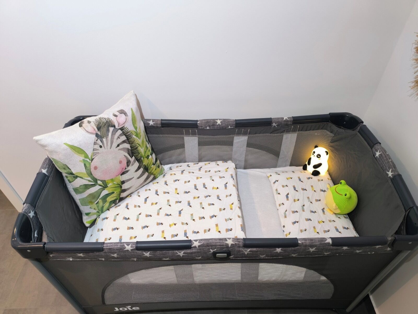 Ein Babybett mit einem Zebra-Kissen, einem Panda-Kissen und einem grünen Spielzeug.