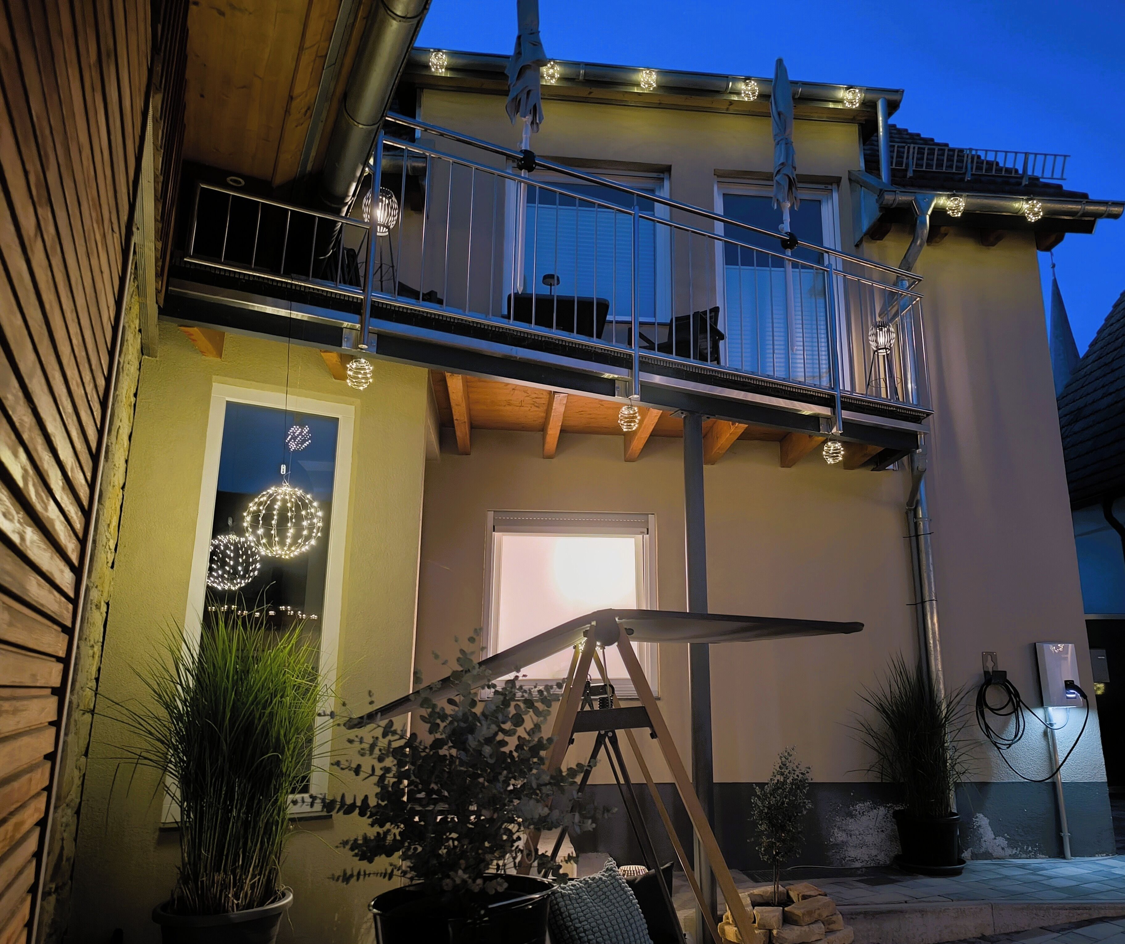 Un edifici amb un balcó, plantes en testos i lluminàries exteriors.