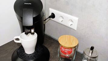 A coffee maker, a jar of coffee, and a bowl of yogurt on a countertop.