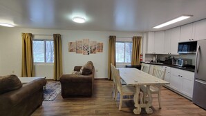 A modern living room with a sofa, ottoman, and dining table. A kitchen with white cabinets and appliances is visible. - LAKEFRONT 2-bedroom Chateau Getaway at Whitecap Mountains Resort Unit 4 (Upson)