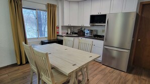 A compact kitchen with white cabinets, a stainless steel refrigerator, a microwave, and a dining table with chairs. - LAKEFRONT 2-bedroom Chateau Getaway at Whitecap Mountains Resort Unit 4 (Upson)