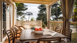 A covered patio with a table and chairs, a bowl of oranges, and a view of trees. - Amazing (sta)caravan in Banjol (Banjol)