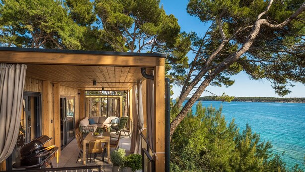 Una cabaña de madera con comedor, mobiliario exterior y vistas al mar.