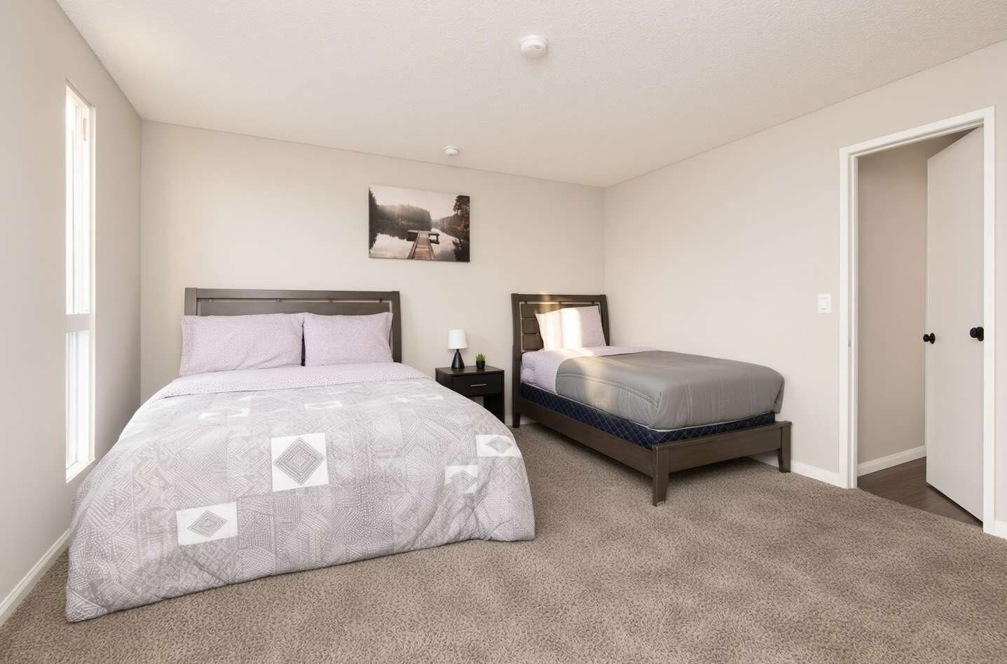 A bedroom with two beds, a nightstand, a lamp, and a picture on the wall.