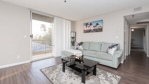 A living room with a sofa, coffee table, and a painting on the wall. - Hollywood 2BR Apt with Rooftop Pool & Cityscape (Los Angeles)