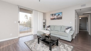 A living room with a sofa, coffee table, and a painting on the wall. - Hollywood 2BR Apt with Rooftop Pool & Cityscape (Los Angeles)