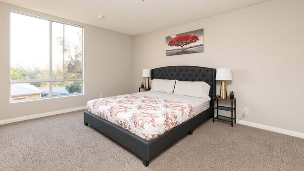 A bedroom with a large bed, a window, and a painting on the wall. - Hollywood 2BR Apt with Rooftop Pool & Cityscape (Los Angeles)