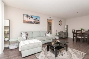 A living room with a sofa, coffee table, and dining area with chairs. - Hollywood 2BR Apt with Rooftop Pool & Cityscape (Los Angeles)