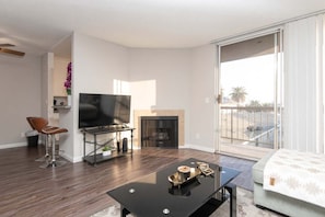 A modern living room with a flat-screen TV, a fireplace, a dining table, and a sofa. - Hollywood 2BR w/ Rooftop Pool & City Views (Los Angeles)