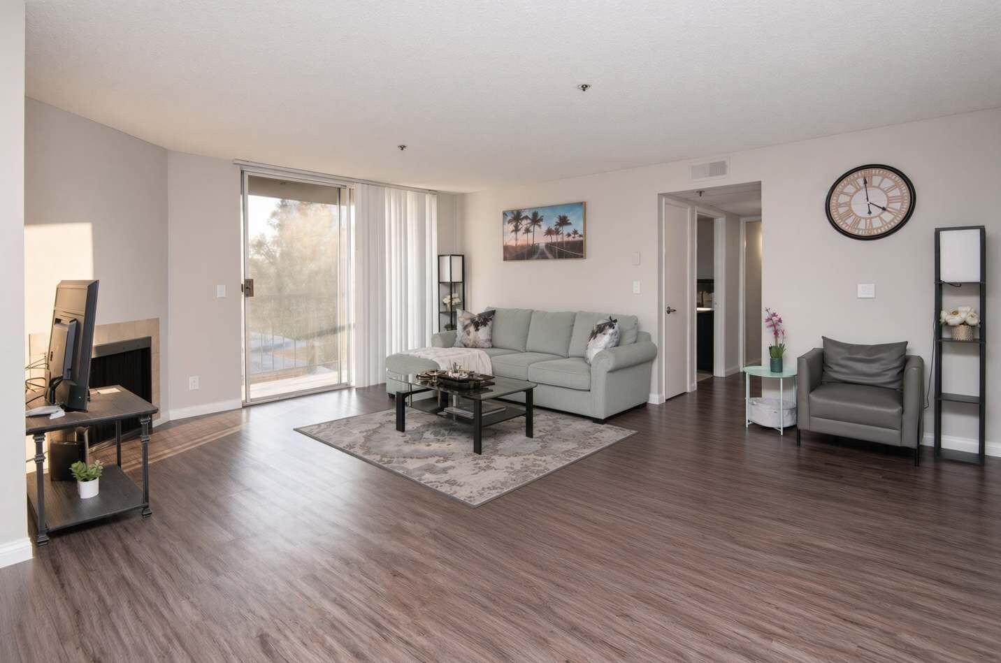 A spacious living room with a large window, a gray sofa, a coffee table, and a fireplace.