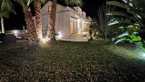 Un edificio moderno con techo plano, rodeado de palmeras y senderos bien iluminados.