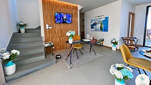 Una sala de estar moderna con una escalera, un televisor de pantalla plana, un comedor y un ventanal grande.