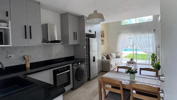 Una cocina moderna con armarios grises, encimera negra y comedor con mesa y sillas de madera.