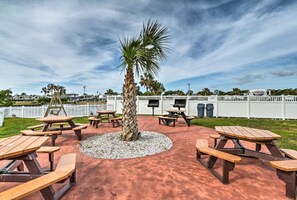 An outdoor patio area with picnic tables arranged around a central palm tree, surrounded by a white fence. - Oceanfront Studio with resort amenities (Myrtle Beach)