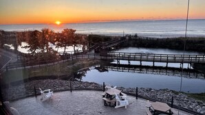 A sunset view from a balcony overlooking a beach, a wooden pier, and a small dock. - Oceanfront Studio with resort amenities (Myrtle Beach)