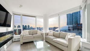 A modern living room with two sofas, a glass coffee table, and large windows offering a city view. - Bright 3BR Downtown Vancouver Condo w/ Pool & Gym (Vancouver)