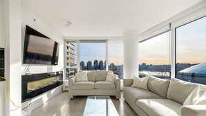 A modern living room with a large TV, two sofas, a coffee table, and a city view through large windows. - Bright 3BR Downtown Vancouver Condo w/ Pool & Gym (Vancouver)