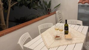 An outdoor dining area with a white table, chairs, a bottle of wine, and a bowl of snacks. - Janas Holiday House: in the heart of southern Sardinia. Sea and real Sardinia. (assemini)