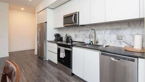 A modern kitchen with stainless steel appliances, a marble backsplash, and a black countertop.