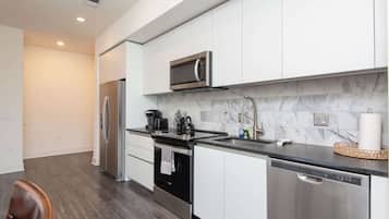 A modern kitchen with stainless steel appliances, a marble backsplash, and a black countertop.